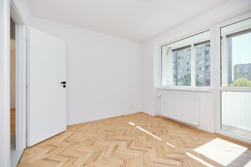 Szoba egy háromszobás lakásban, fa dekoros padlóval és nagy ablakkal.