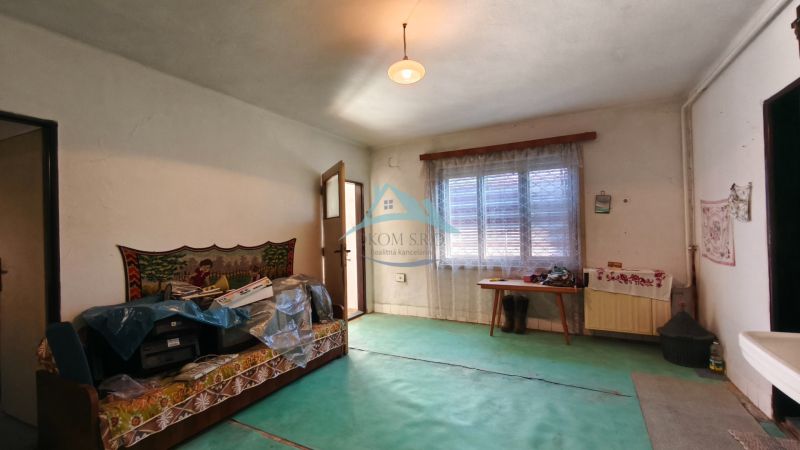 Szoba egy családi házban szőnyegpadlóval, kanapéval és függönyös ablakkal.