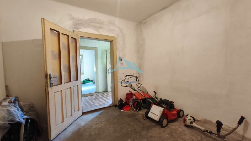 Családi ház belső tere nyitott ajtókkal, fűnyíróval és szerszámokkal a padlón.