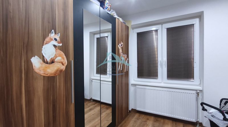 Állatmintás szekrény a családi házban, fa padló, radiátor az ablak alatt redőnyökkel.