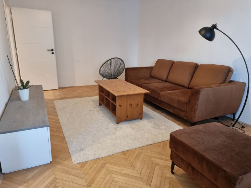 Nappali egy kétszobás lakásban, barna kanapé, dohányzóasztal, fa mintázatú padló.
