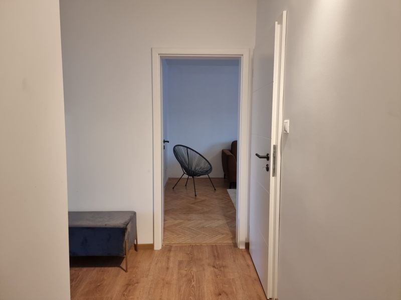 Kétszobás lakás folyosója fa mintás padlóval és kilátással a nappalira.
