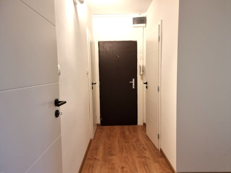 Folyosó egy kétszobás lakásban, fa mintázatú padlóval és fehér ajtókkal.