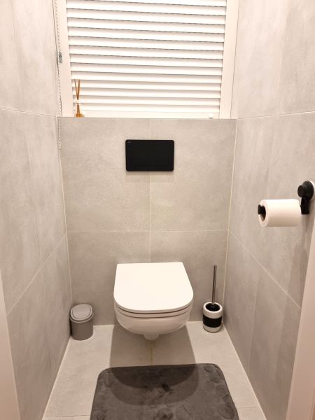 Fürdőszoba egy kétszobás lakásban modern függesztett WC-vel világos csempéken.