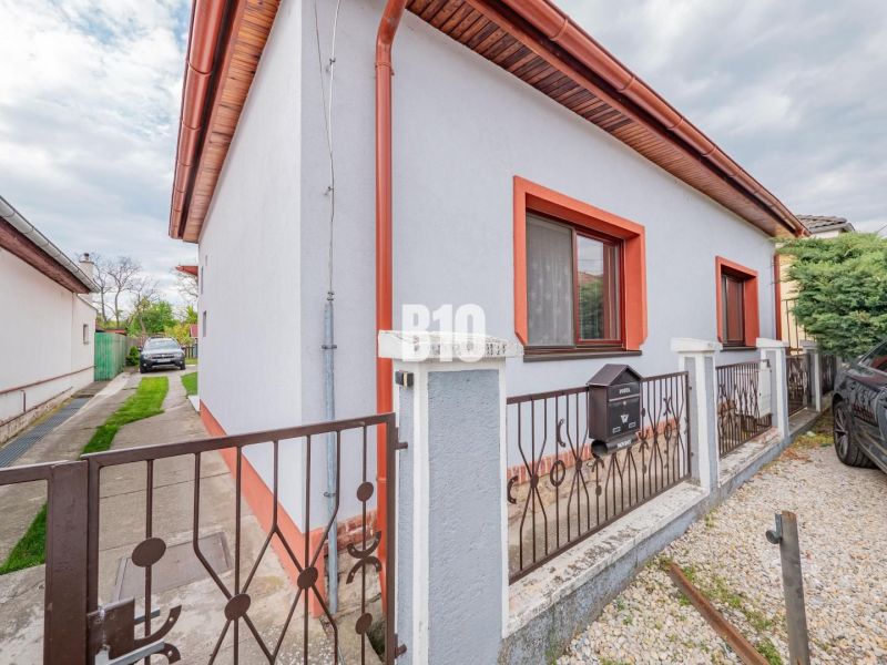 Családi ház Nyitrán fehér homlokzattal, piros szegéllyel és kerttel.