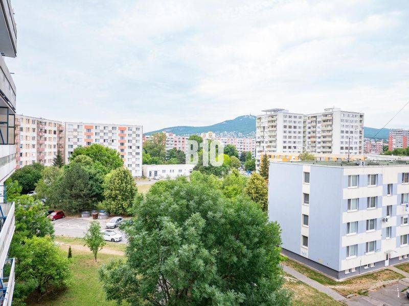 Kilátás egy háromszobás lakásból Nyitrán panelházakra és parkolóra autókkal.
