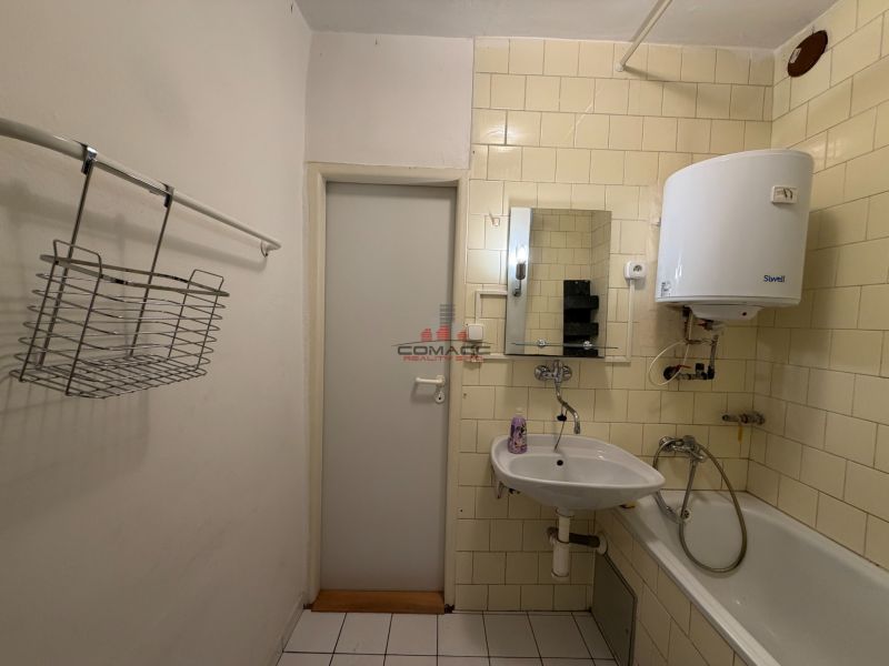 Fürdőszoba egy háromszobás lakásban mosdóval, káddal és a falon lévő vízmelegítővel.