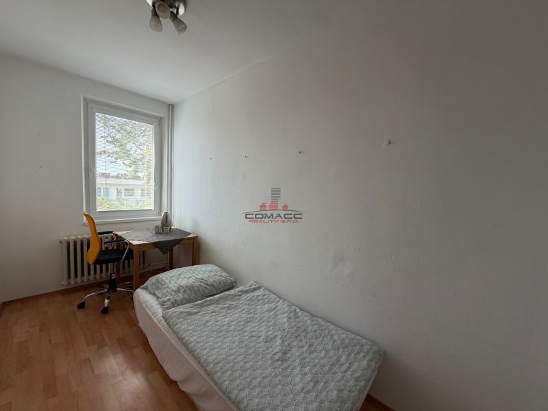 Szoba egy háromszobás lakásban ággyal, asztallal és fa dekorációjú padlóval.