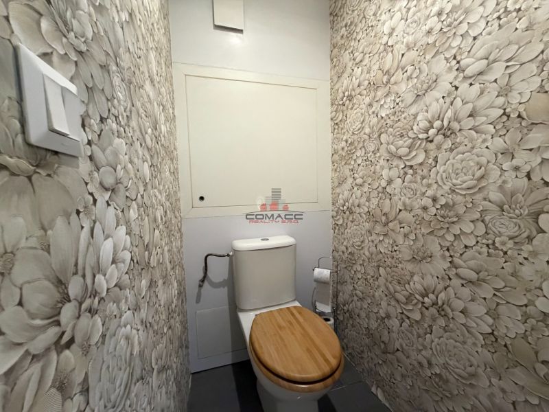 Virágmintás tapétával és fa ülőkével ellátott WC egy háromszobás lakásban.