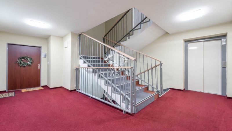 Folyosó a Rekreációs apartmanban piros szőnyeggel, lépcsőházzal és lifttel.