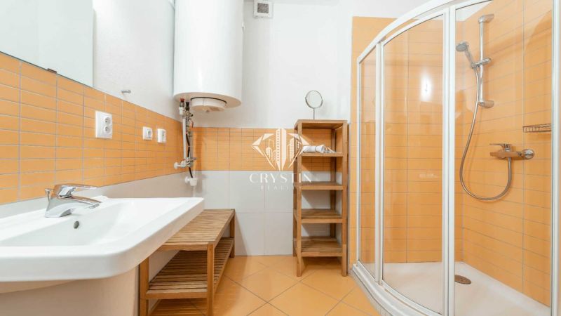 Fürdőszoba narancssárga csempékkel, zuhanyzóval és mosdóval egy nyaraló apartmanban.