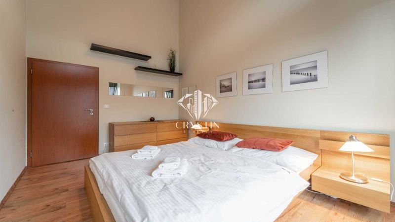 Világos hálószoba egy nyaraló apartmanban, fa dekoros padlóval és egyszerű berendezéssel.