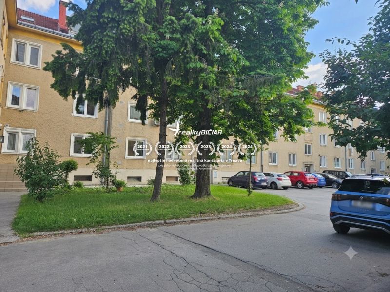 Parkoló a háromszobás lakásoknál a Trnava-i Študentská utcán, zölddel és fákkal körülvéve.