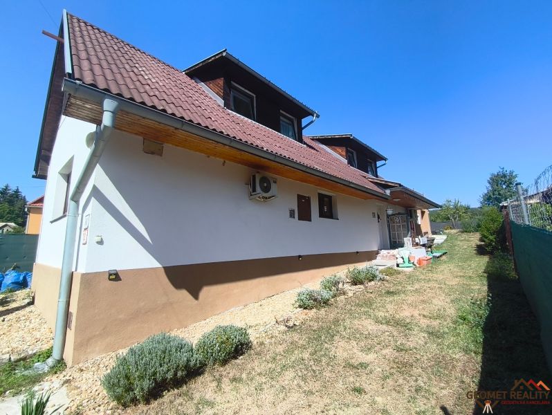 Családi ház Divínban barna tetővel és kerttel, gyep és bokrok szegélyezik.