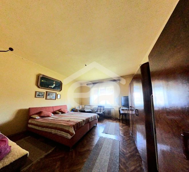 Hálószoba családi házban fa dekoros padlóval, ágy, szekrények, képek a falon.