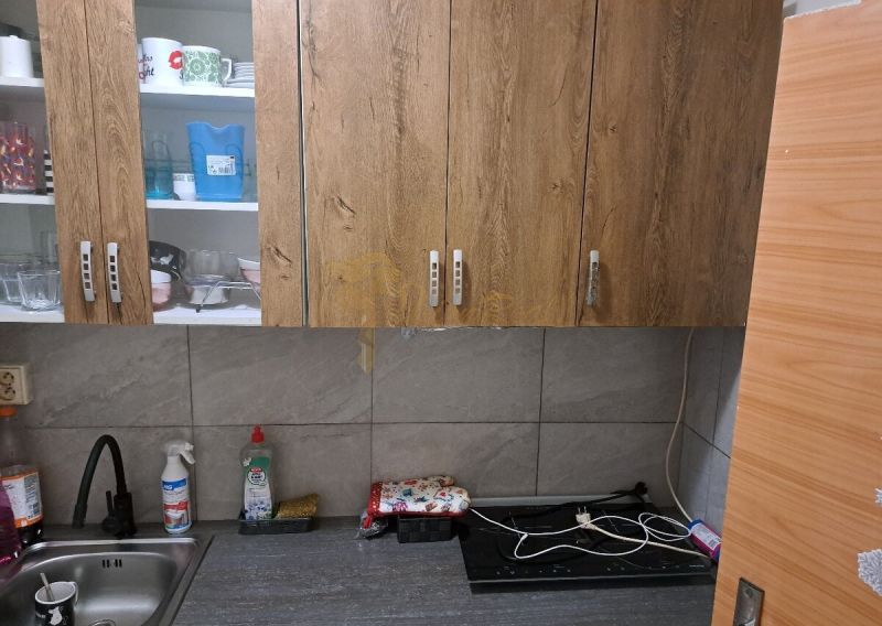 Konyha fa szekrényekkel, mosogatóval és munkalappal egy garzonlakásban.