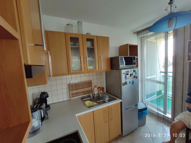 Konyha fa szekrényekkel, mikrohullámú sütővel és hűtőszekrénnyel egy kétszobás lakásban.