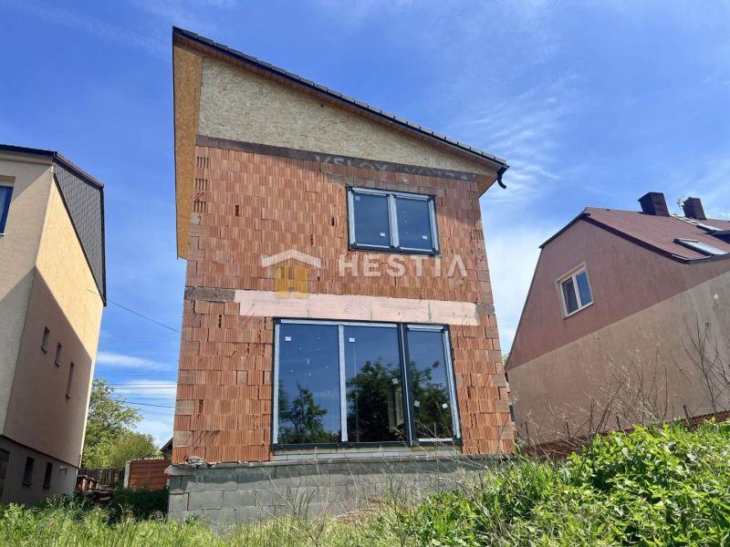 Családi ház Cerován befejezetlen téglahomlokzattal és nagy üvegajtókkal.