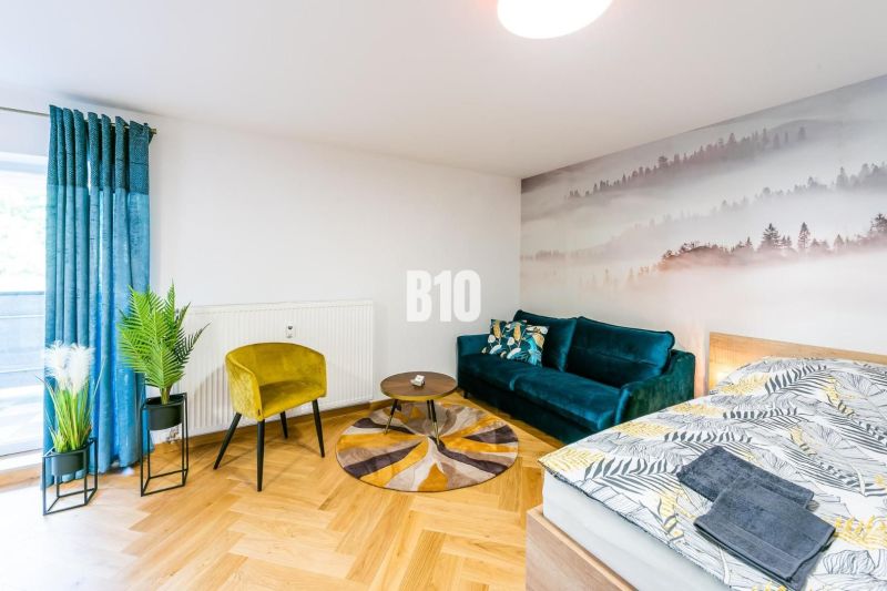 Stílusos nyaraló apartman fa hatású padlóval, kanapéval és növényekkel.