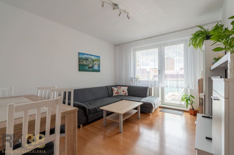 Világos nappali egy háromszobás lakásban, fa dekorációjú padlóval és kanapéval.