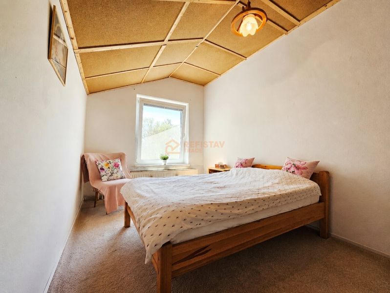 Hálószoba családi házban, fa mennyezettel, szőnyeggel és párnákkal ellátott ággyal.