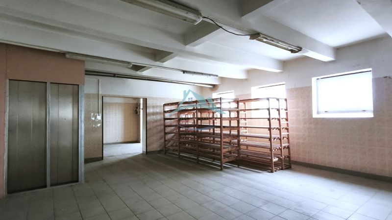 Gyártóhelyiségek polcokkal és lifttel, ablakokkal megvilágítva, kerámia padlóval.