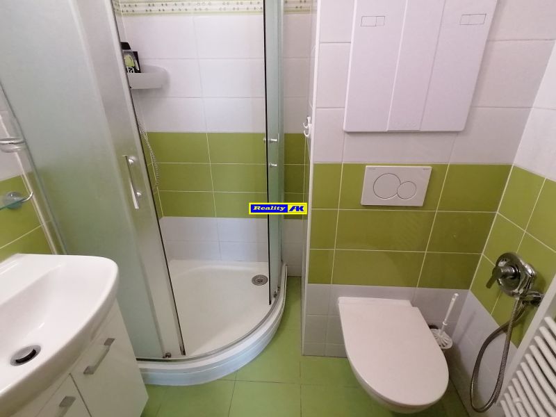 Fürdőszoba zuhanyzóval és zöld csempékkel egy kétszobás lakásban.