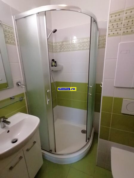 Fürdőszoba zuhanyzóval és zöld csempékkel egy kétszobás lakásban.