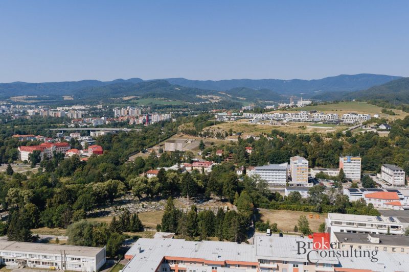 Kilátás Besztercebánya panorámájára a Komenského utcáról, láthatók családi házak és a természet.