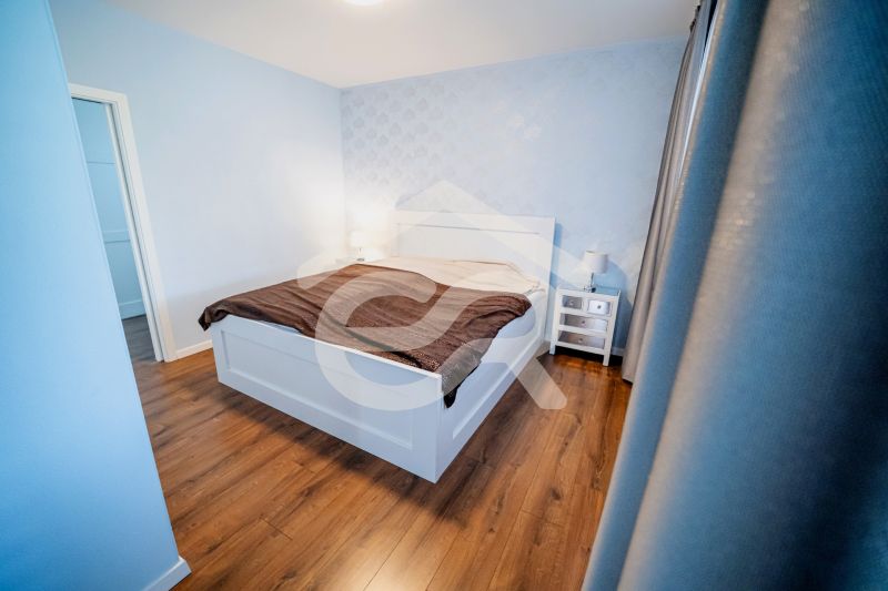 Hálószoba családi házban ággyal, éjjeliszekrényekkel és fa mintázatú padlóval.