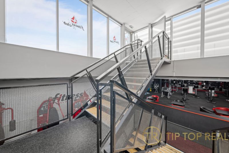 Kétszintes üzlethelyiség acéllépcsővel és fitneszberendezésekkel.