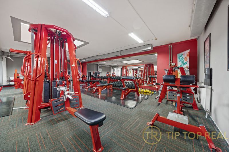 Fitneszközpont piros edzőgépekkel és súlyzókkal, üzlethelyiségek.