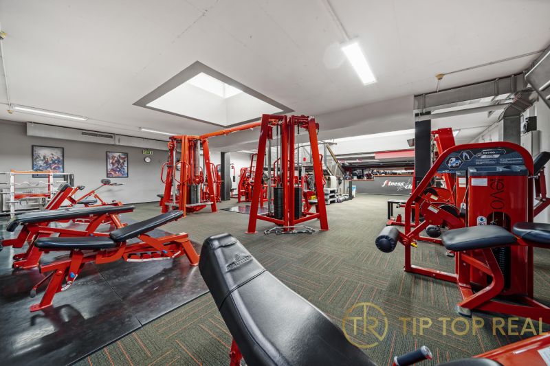 Fitneszközpont erősítő gépekkel és piros padokkal, alkalmas üzlethelyiségek.