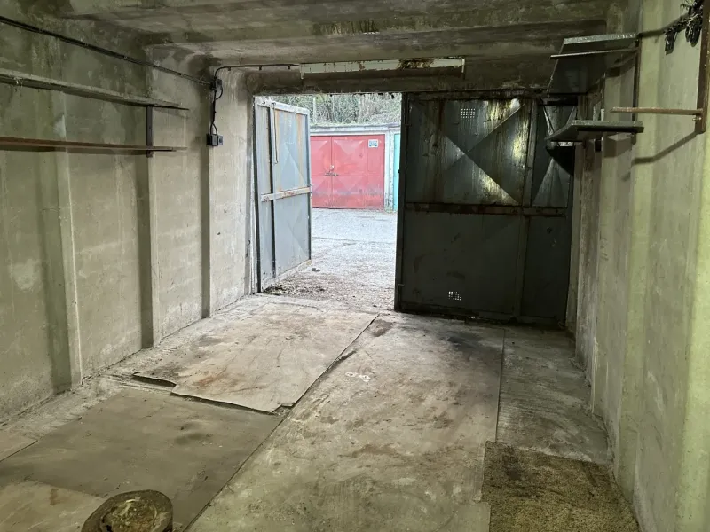 Betongarázs nyitott acélajtókkal, kilátás egy másik garázsra kívül.