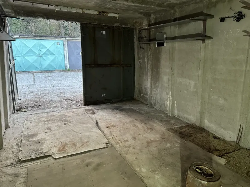 Garázs belső tér betonpadlóval és fém polcokkal.