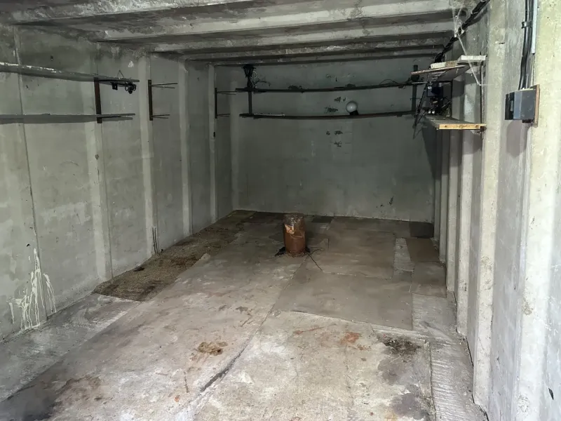 Garázs belső tér betonfalakkal és tárolópolcokkal.