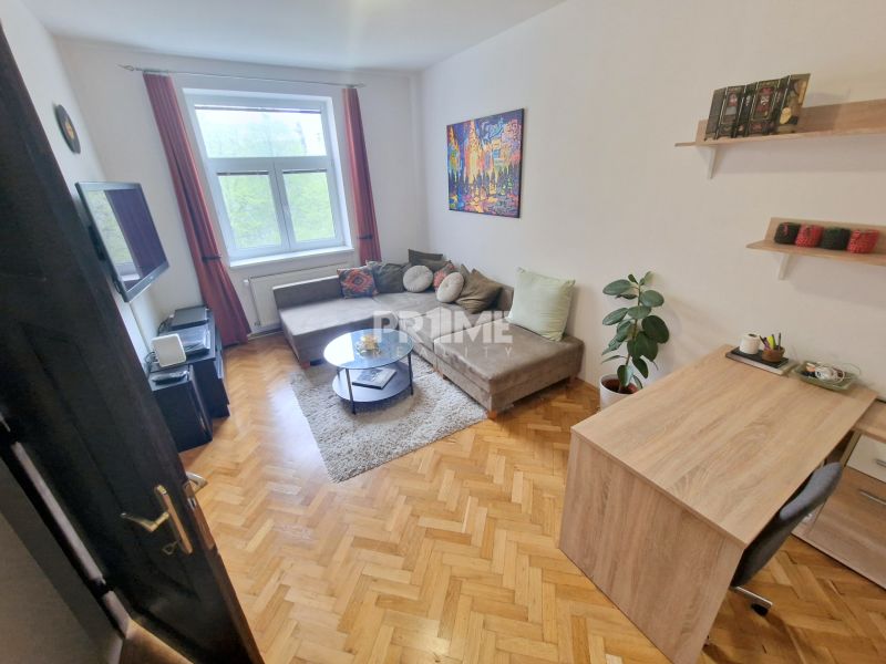 Egy háromszobás lakás szobája kanapéval, televízióval és fa dekorációjú padlóval.