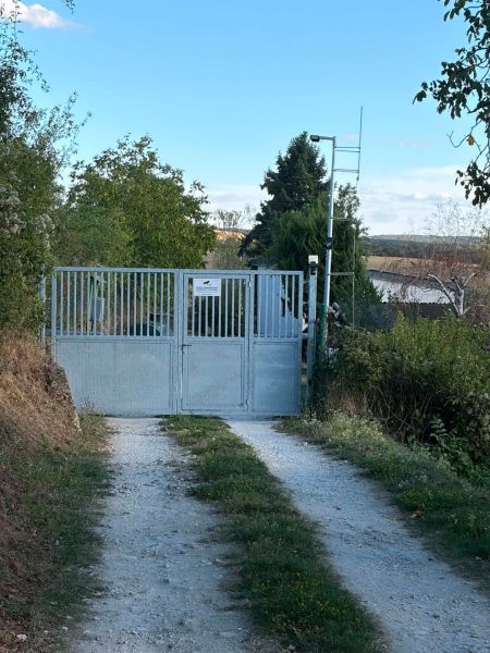 A Banka-i házhoz vezető kapu, amelyet zöld növényzet és földút vesz körül.