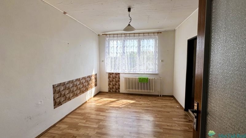 Egy szoba családi házban fa dekorációjú padlóval, függönnyel és radiátorral az ablak alatt.