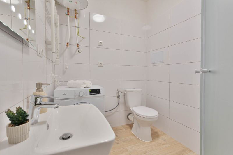 Fürdőszoba a garzonlakásban mosógéppel, mosdóval, WC-vel és zuhanyzóval, fa dekoros padlóval.