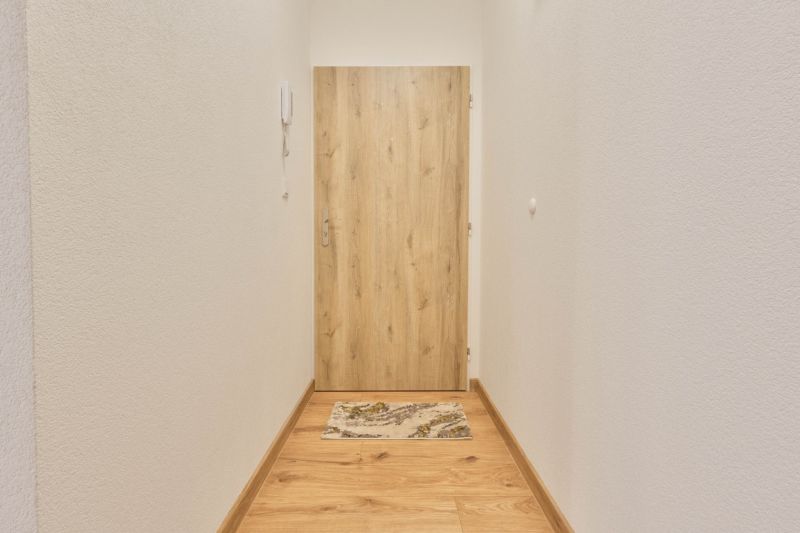 Keskeny folyosó fehér falakkal és fa dekorációjú ajtókkal a garzonlakásban.