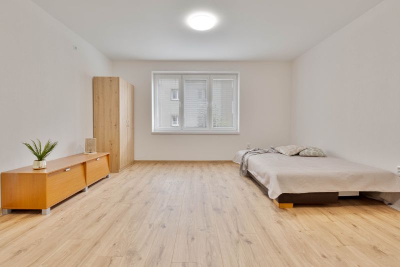 Egy garzonlakás fa mintázatú padlóval, ággyal és szekrénnyel, semleges színekben.