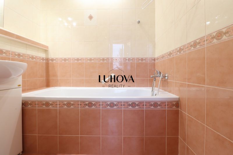 Fürdőszoba egy kétszobás lakásban káddal és mosdóval, bézs és rózsaszín csempével burkolva.