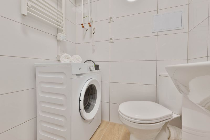 Fürdőszoba garzonlakásban mosógéppel, WC-vel és fa dekoros padlóval.