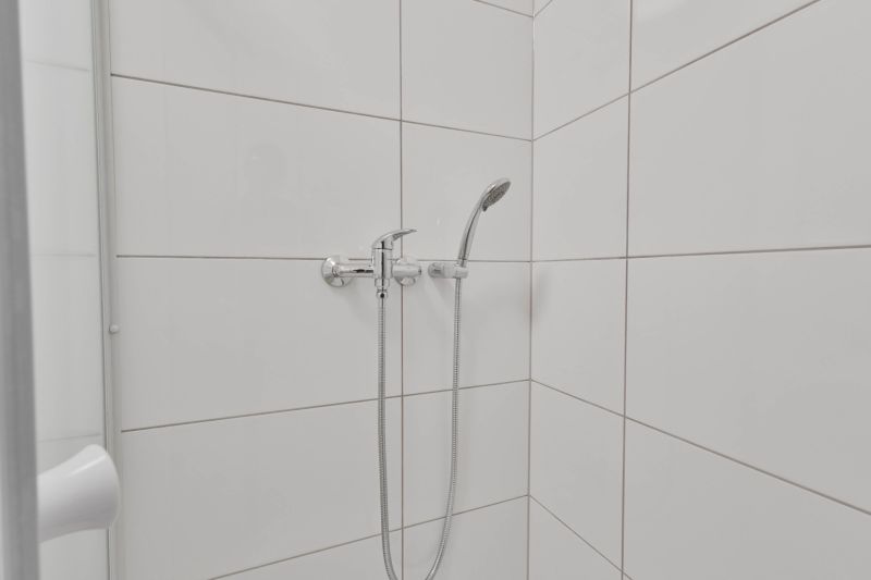Zuhanykabin fehér csempékkel és zuhanyfejjel a garzonlakásban.