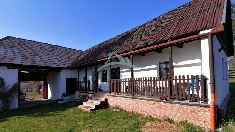 Családi ház verandával, fa gerendákkal, téglából készült alappal és nagy füves kerttel.
