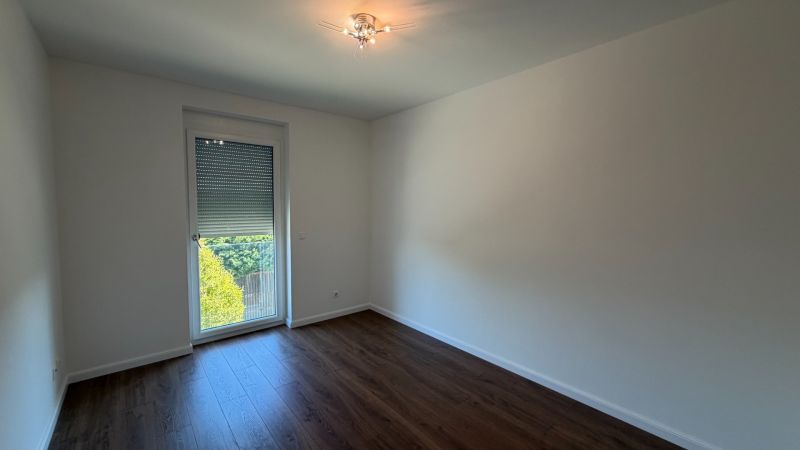 Szoba egy háromszobás lakásban fehér falakkal és fa dekoros padlóval.