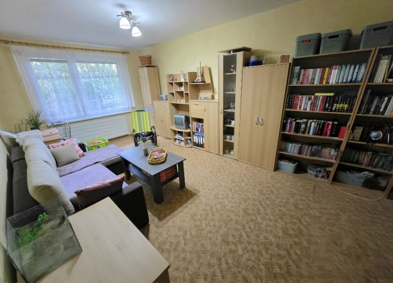 Nappali egy 4 szobás lakásban nagy kanapéval, asztallal és könyvespolccal.