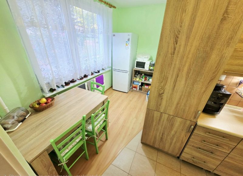 Konyha egy 4 szobás lakásban asztallal, zöld székekkel és fa dekorációjú padlóval.