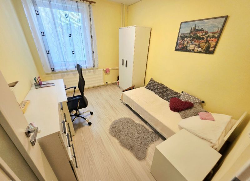 Sárga szoba egy ággyal, íróasztallal és fa dekorációjú padlóval egy 4 szobás lakásban.